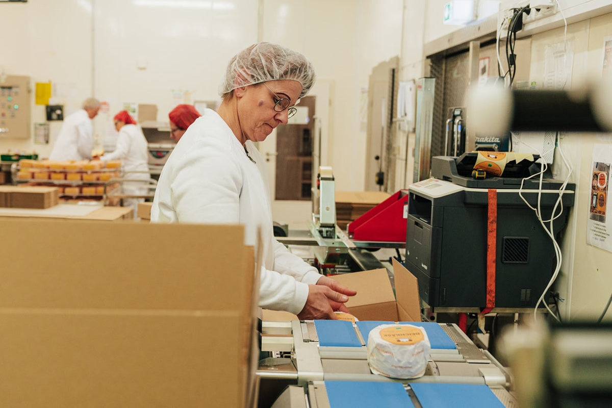 Eine Frau steht in der Versandabteilung vom Backensholzer Hof und verpackt ein Käsepaket