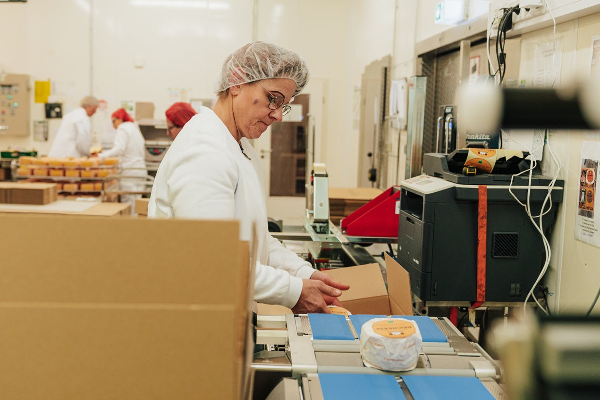Eine Frau steht in der Versandabteilung vom Backensholzer Hof und verpackt ein Käsepaket