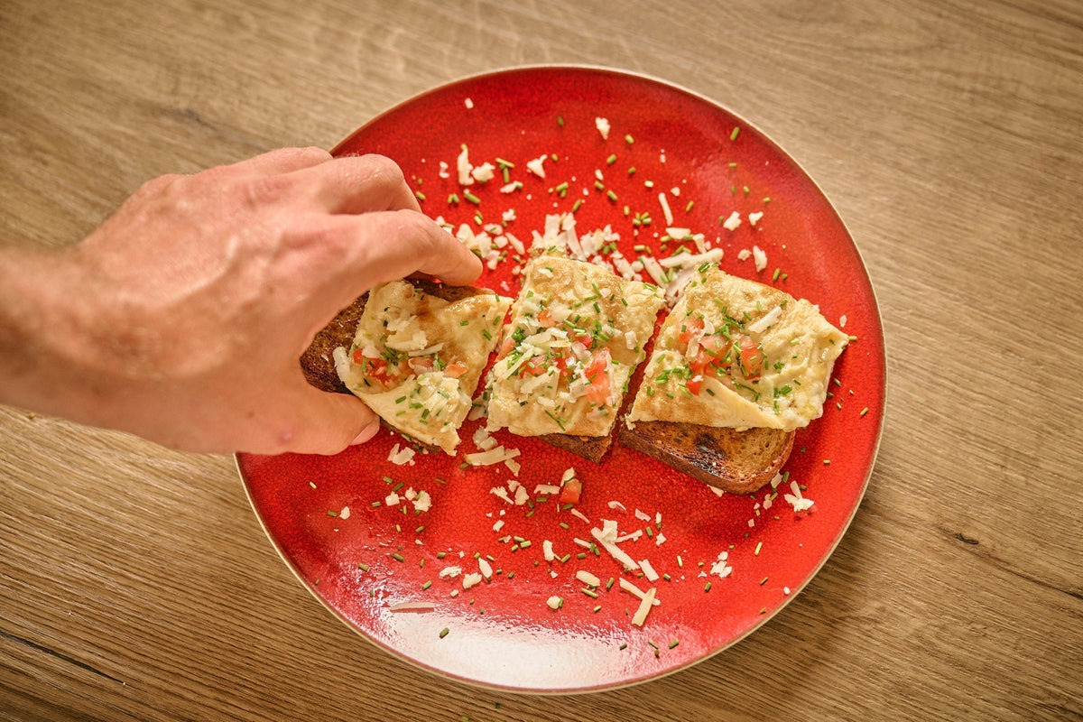 Auf einem roten Teller liegt ein Brot mit einem Omelett und eine Hand greift danach