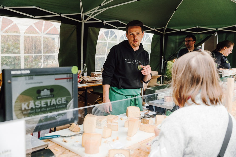 Ein Mann steht in einem Verkaufszelt und verkauft Käse.