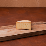 Halber Laib Käse auf Holzbrett.