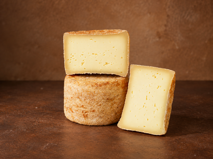 Der Käse Sturmkäse liegt ganz und halbiert auf einem braunen Hintergrund