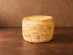 Der Käse Sturmkäse liegt als ganzer Laib auf einem braunen Hintergrund