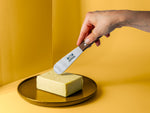 Butter mit Backensholz Logo in Hand gehalten über einem Stück Butter auf braunem Teller.