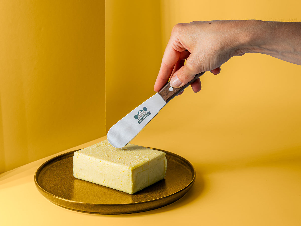 Butter mit Backensholz Logo in Hand gehalten über einem Stück Butter auf braunem Teller.