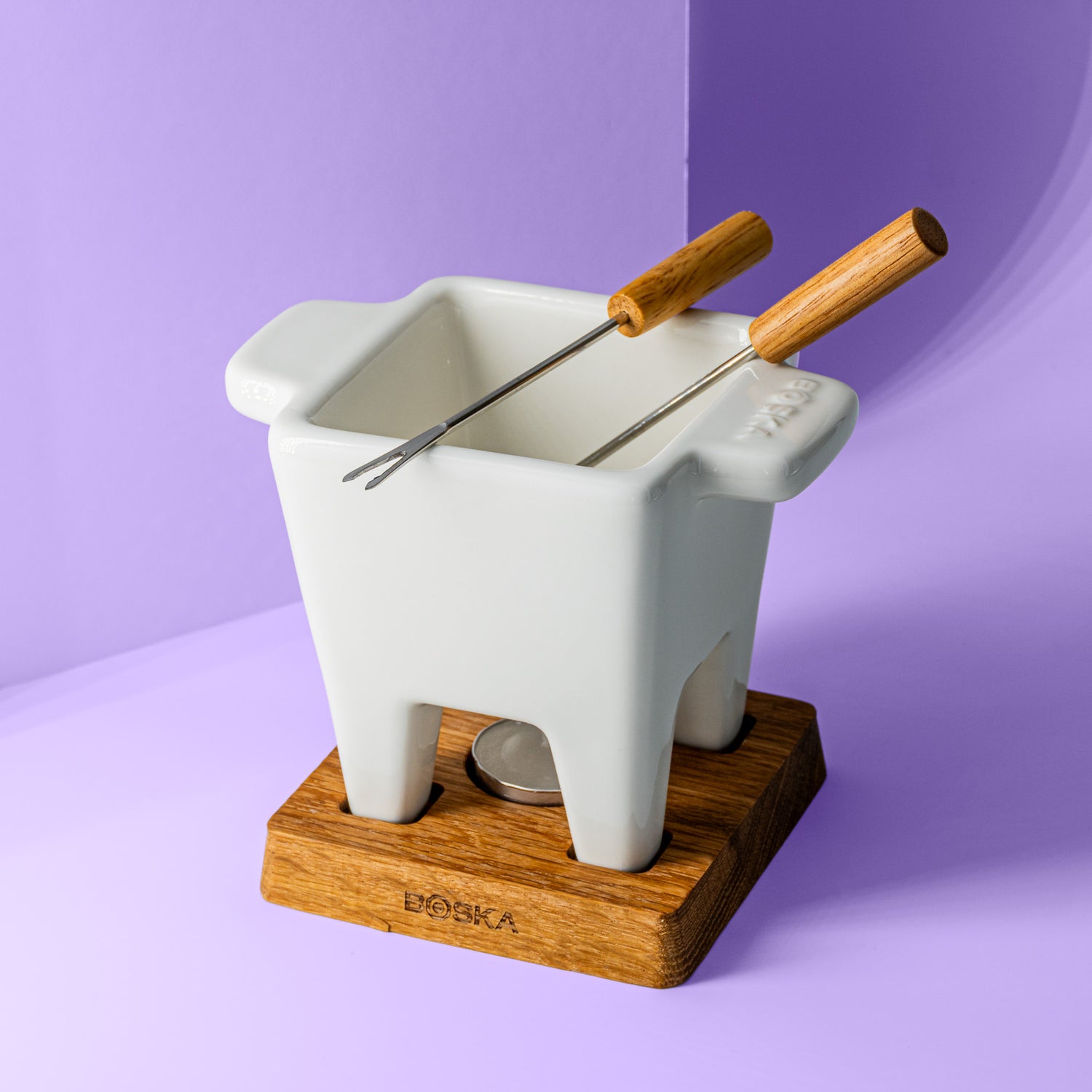 Käsefondue Topf, zwei Bestecke mit Holzgriffen, einem Holzuntersetzer drunter für Teelicht.