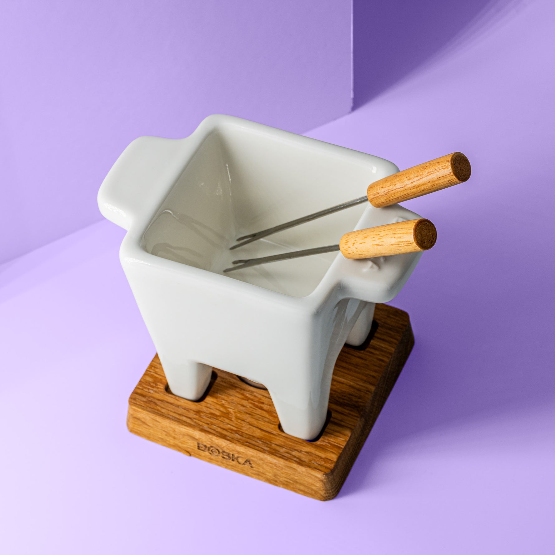 Käsefondue Topf, zwei Bestecke mit Holzgriffen, einem Holzuntersetzer drunter für Teelicht.