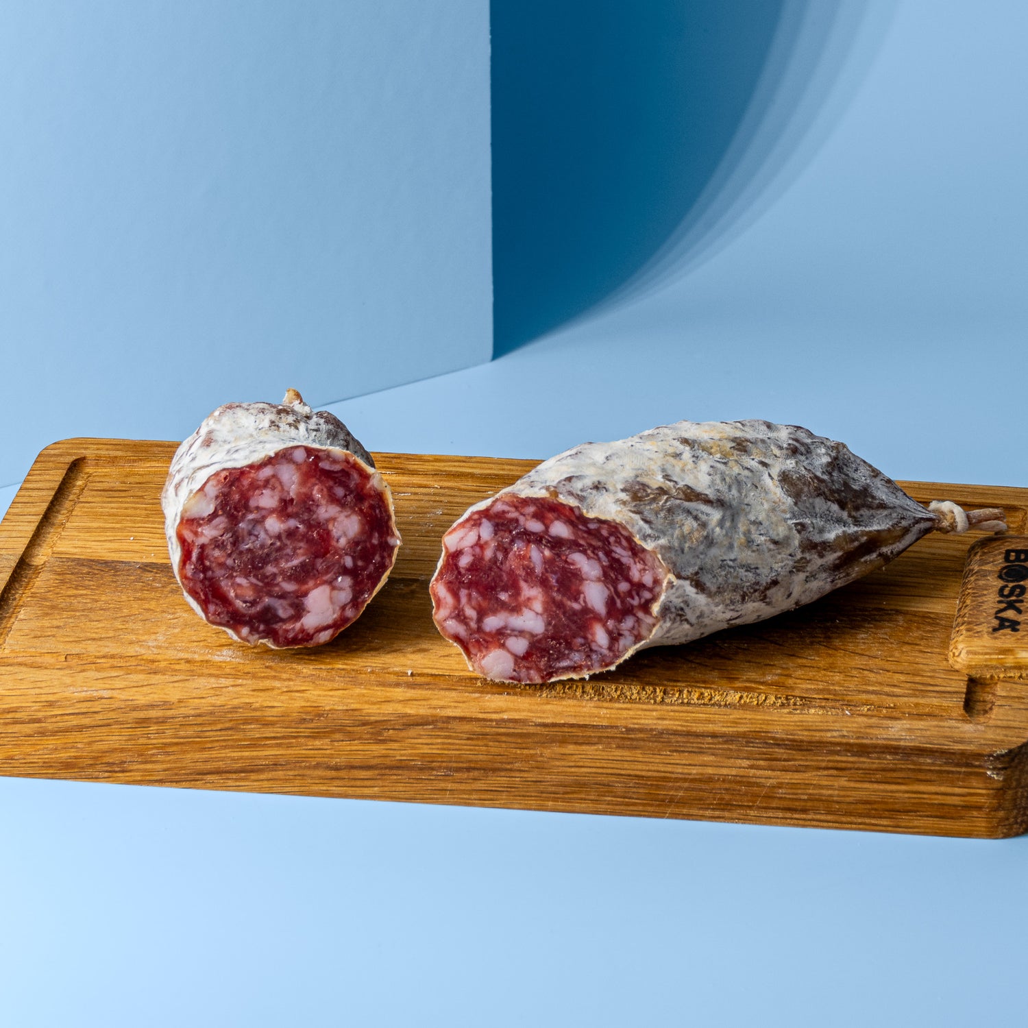 Salami in zwei Stücke geschnitten auf Holzbrett.